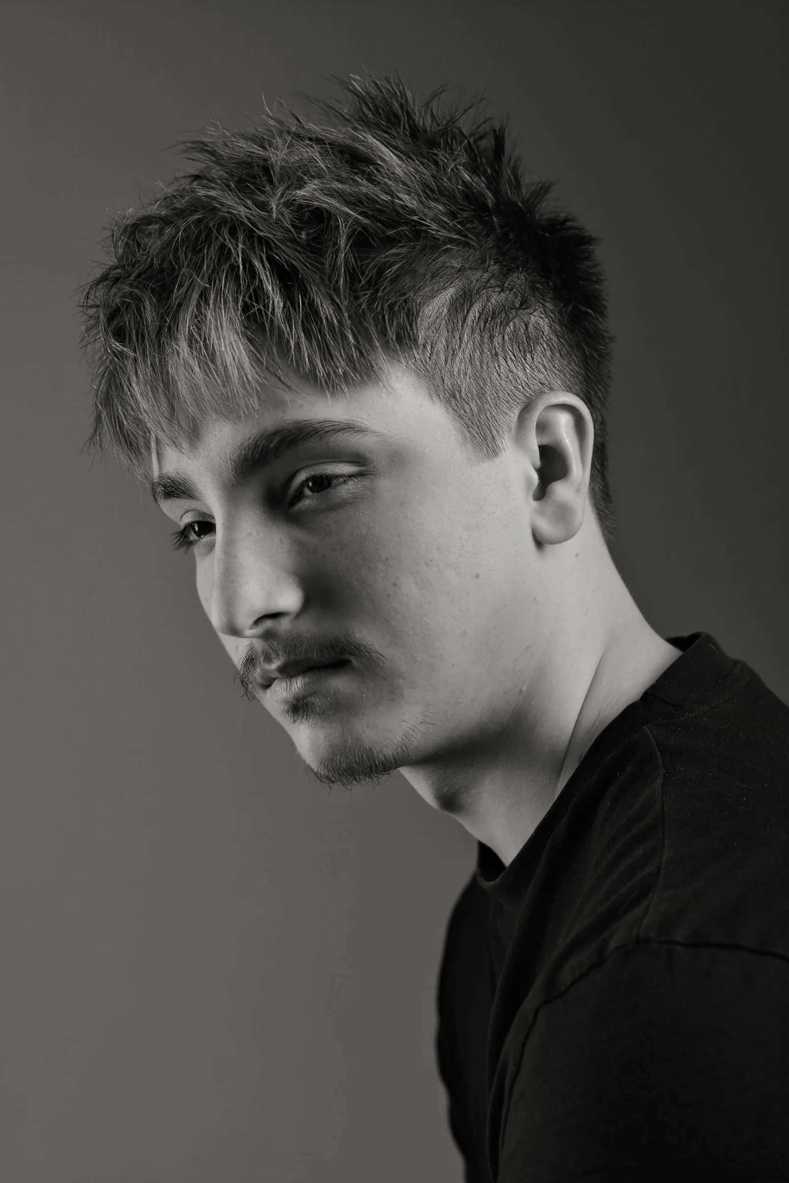 Choppy textured fringe with lightened tips and short faded sides, the head turned down and away