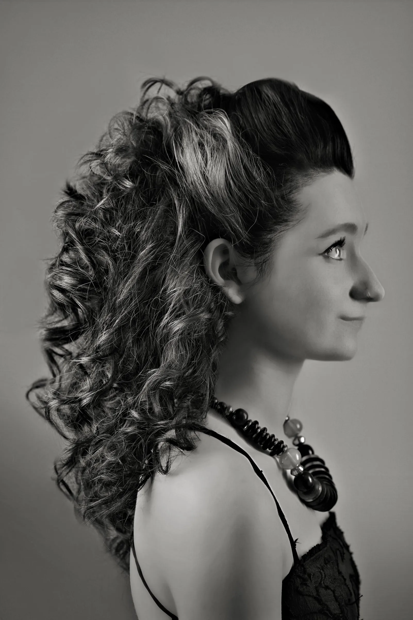 Hair swept back from the face into a high, cascading mass of ringlet curls, seen in side profile