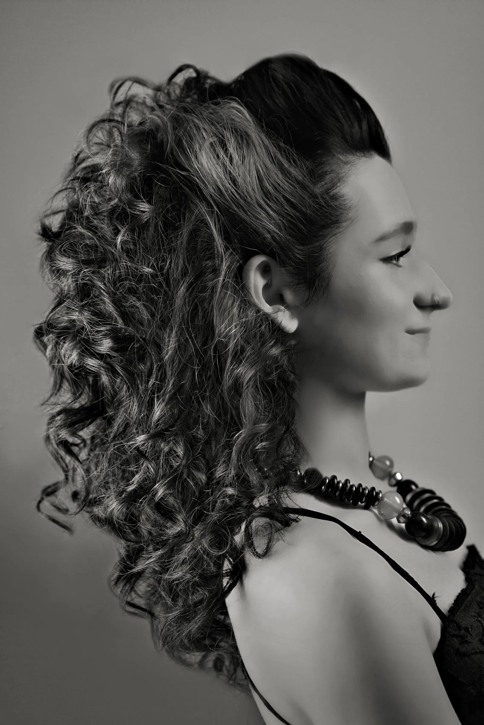 Ringlets falling past the shoulder from a high curled style, in a closer profile with the model smiling