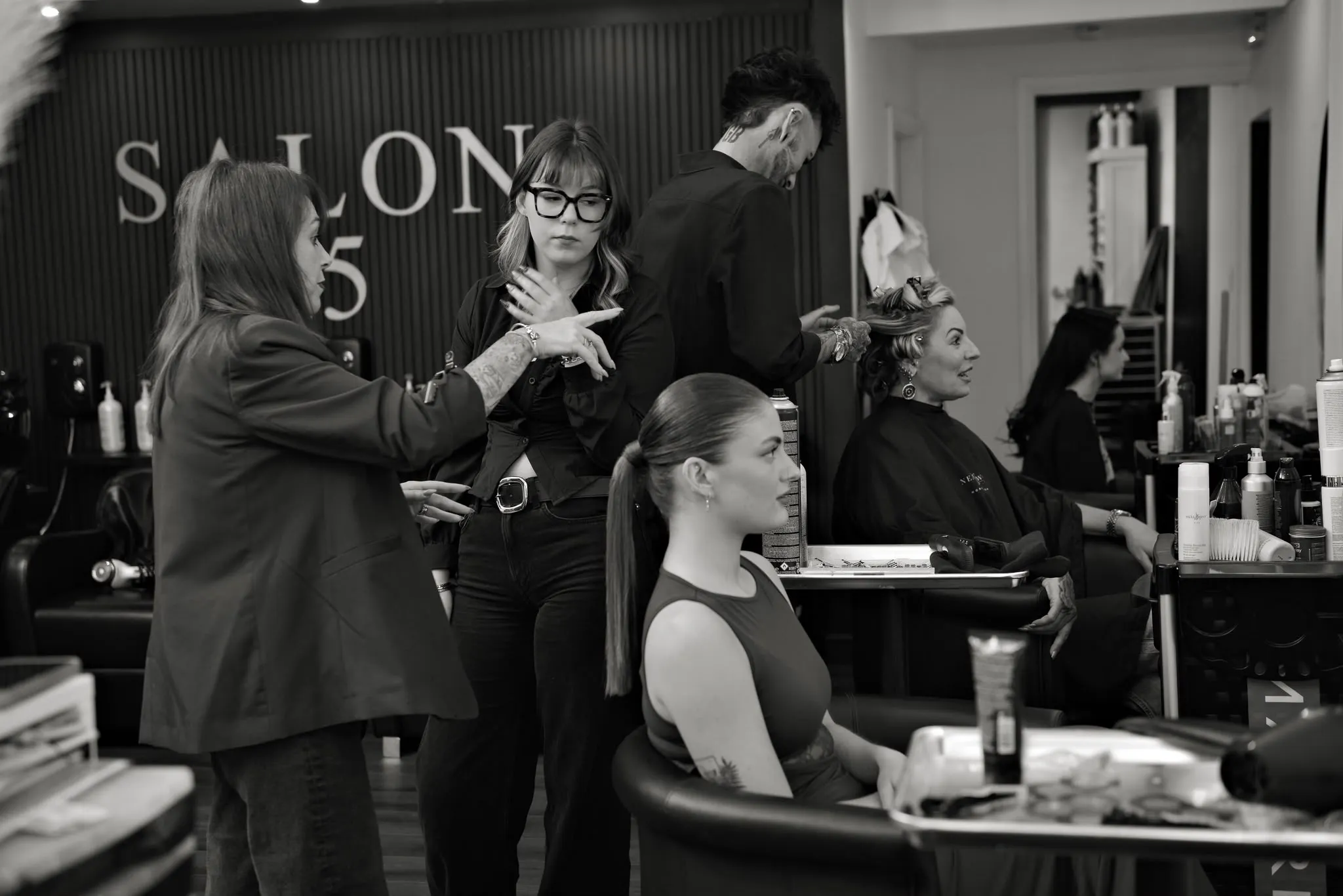 The Salon 15 team at work: Katie, Kennedi and AJ, with a client in the foreground and the SALON 15 wall behind