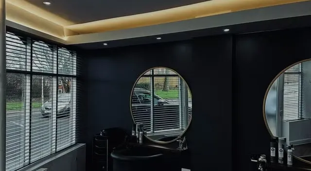 Inside Salon 15, Normanton: round gold-framed mirrors on a near-black wall with warm cove lighting and oak counters